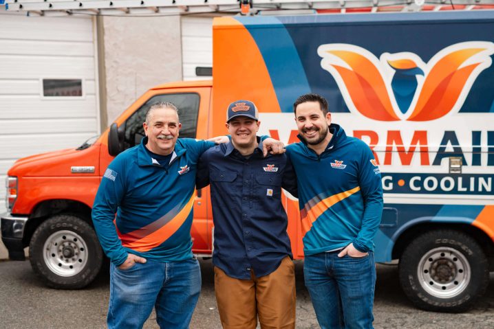 Three men smiling in front of van.